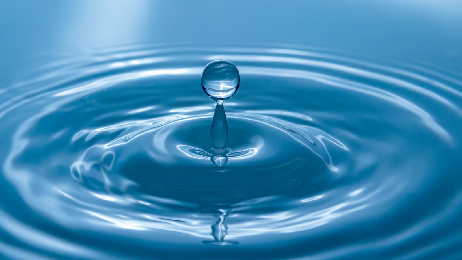 Wassertropfen fällt auf eine blaue Wasseroberfläche und zieht Kreise